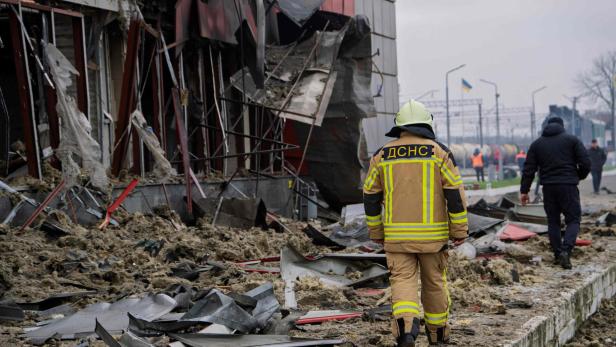 Ein Feuerwehrmann mit der Aufschrift "ДСНС" steht vor einem zerstörten Gebäude.