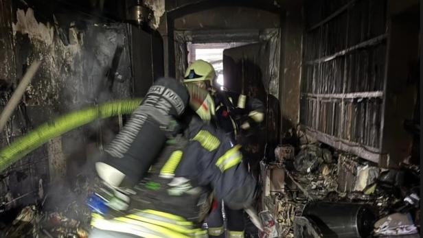 Feuerwehrleute mit Atemschutzgeräten löschen einen stark verbrannten Raum in einem Mehrparteienhaus in Klosterneuburg.