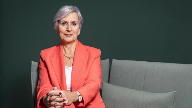 Anna Sporrer sitzt auf einem grauen Sofa vor einem grünen Hintergrund.