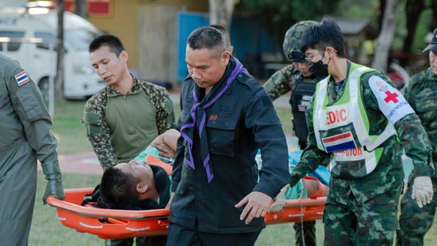 Mehrere Rettungskräfte in Uniform tragen eine verletzte Person auf einer Trage über eine Wiese.