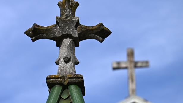 Ein steinernes Kreuz mit Moos im Vordergrund, im Hintergrund ein weiteres Kreuz vor blauem Himmel.