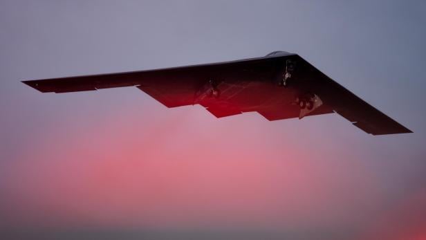 B-2 Stealth-Bomber im Flug bei Sonnenuntergang mit ausgefahrenem Fahrwerk.