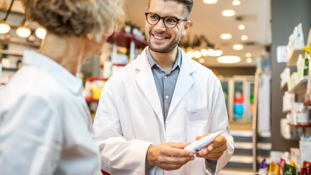 Ein Apotheker berät in einer Apotheke und hält ein Produkt in der Hand. 