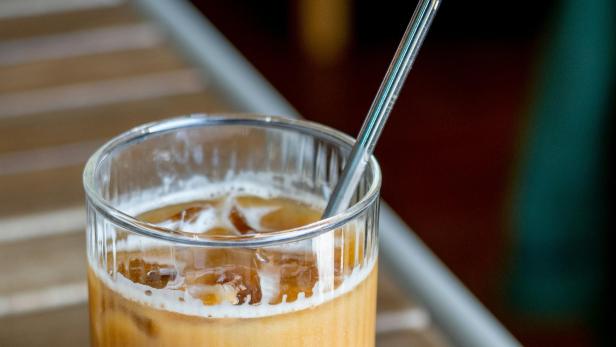 Glas mit Iced Coffee und einem Glasstrohhalm steht auf einem Holztisch