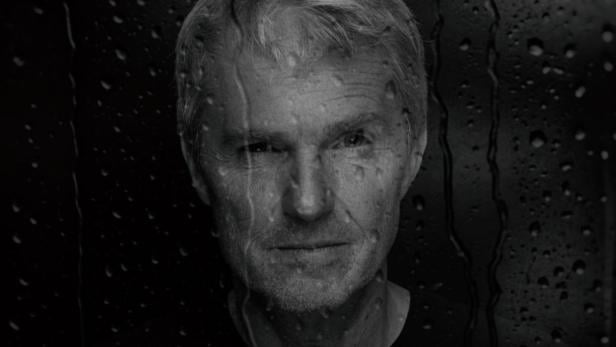 Ein Mann mit Kamera hinter einer nassen Glaswand