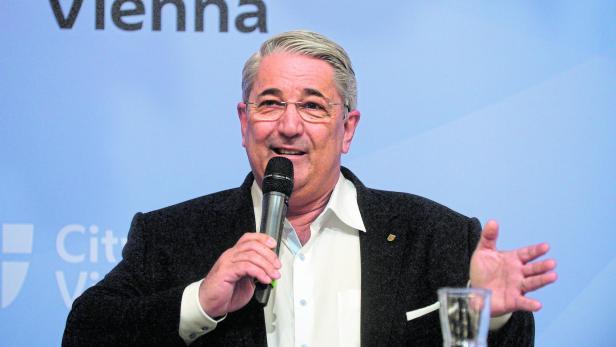 Bezirksvorsteher Nevrivy mit einer Brille, er hat ein Mikrofon in der Hand. 