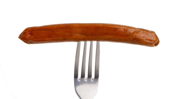 Eine gebratene Wurst steckt auf einer silbernen Gabel vor weißem Hintergrund.