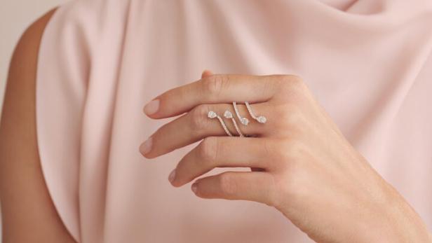 Eine Frau im rosa Kleid mit einem silbernen Ring am Finger, den sie in die Kamera hält