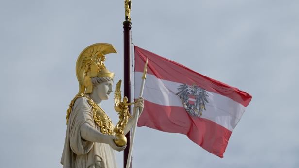 Eine Statue mit goldenen Verzierungen steht vor einer wehenden rot-weiß-roten Flagge mit Adler.