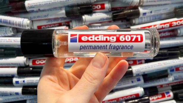 Eine Hand hält einen Flakon des limitierten Edding 6071 Parfums vor einem Hintergrund aus Edding-Markern.