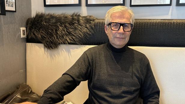 Ein älterer Mann mit Brille sitzt an einem Tisch mit Unterlagen und schaut freundlich in die Kamera.