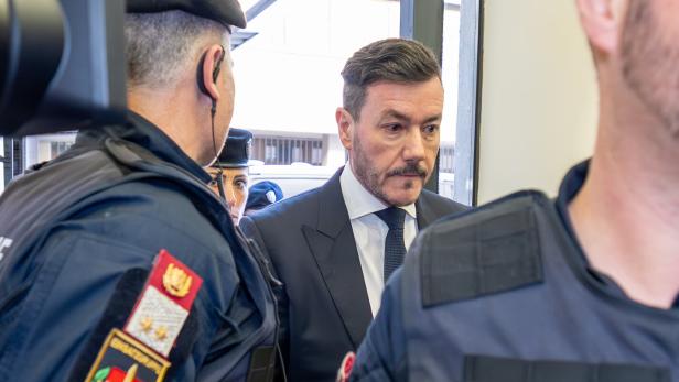 Rene Benko wird von Justizwachebeamten flankiert.