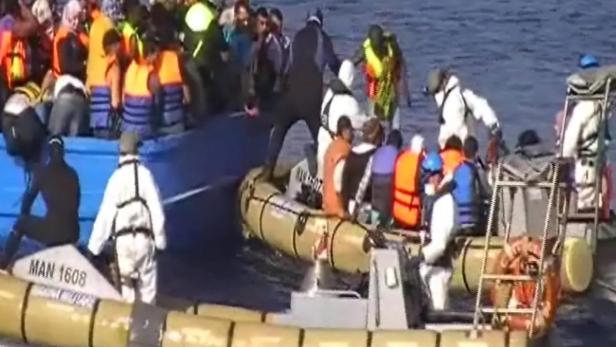 Mehrere Menschen in Rettungswesten steigen von einem Boot in ein anderes.