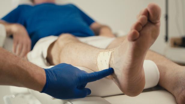 Ein Fuß mit Verband wird von einer Person mit blauen Handschuhen untersucht.