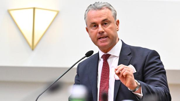 Ein Mann im Anzug spricht an einem Rednerpult mit Mikrofon, im Vordergrund stehen mehrere Flaschen.