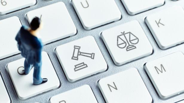 Eine kleine Figur steht auf einer Computertastatur mit Tasten, die Richterhammer und Waage zeigen.