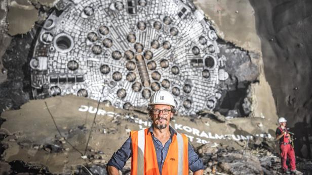 Ein Mann mit Bauhelm und in oranger Warnweste steht vor Tunnelbohrgerät