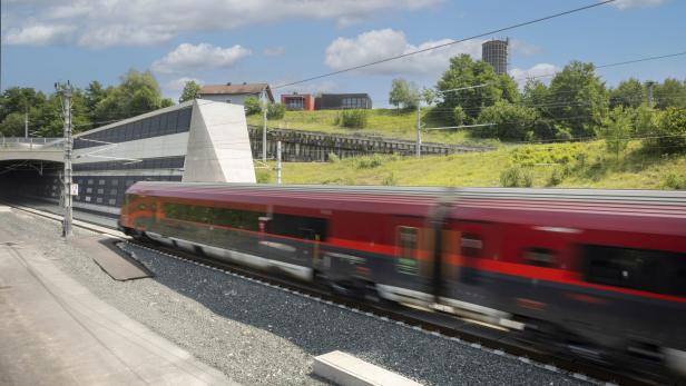 Roter Zug fährt an einem Tunnel und grünen Hügeln unter blauem Himmel vorbei.