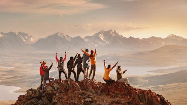 Mehrere Personen stehen auf einem Berggipfel und jubeln 