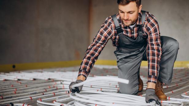 Handwerker verlegt weiße Rohre für eine Fußbodenheizung in einem Neubau.