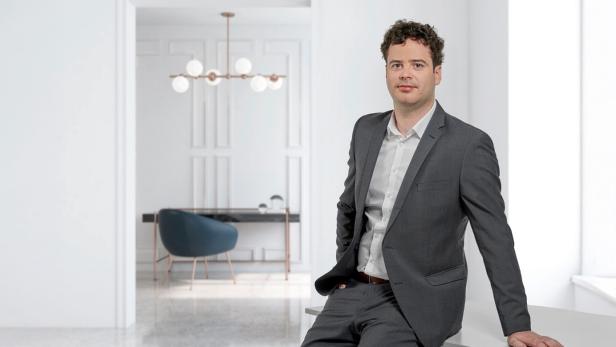 Mann im Anzug lehnt an einem Tisch in modernem, hell eingerichtetem Büro.