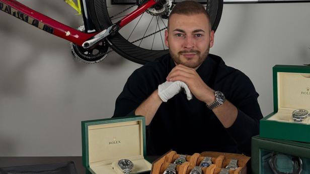 Mann sitzt vor mehreren Luxusuhren, darunter Rolex-Modelle in offenen Uhrenboxen.