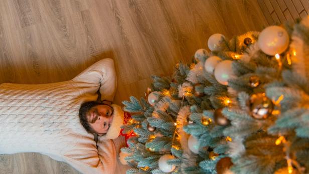 Mann liegt mit Weihnachtshaube und beigen Pullover unter einem Weihnachtsbaum