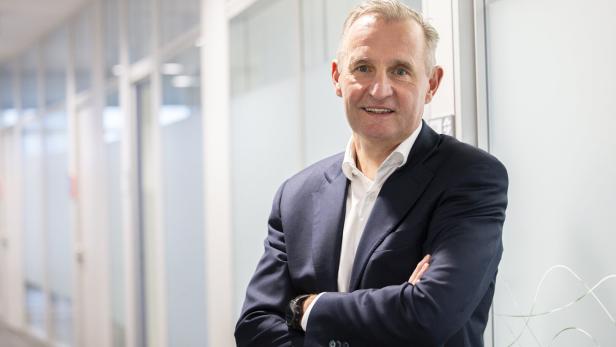 Peter Weinelt steht im Anzug mit gekreuzten Armen in seinem Büro.