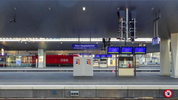 Bahnsteig am Wiener Hauptbahnhof mit Anzeigetafeln, rotem ÖBB-Zug und moderner Überdachung.
