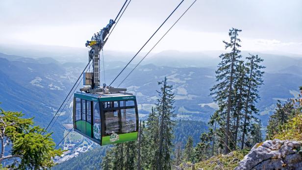 Eine grüne Rax-Seilbahn schwebt vor einer Berglandschaft.