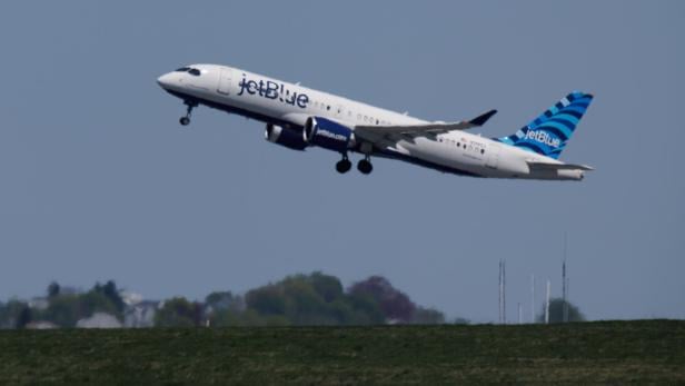 Ein JetBlue-Flugzeug hebt vor blauem Himmel und grüner Landschaft ab.