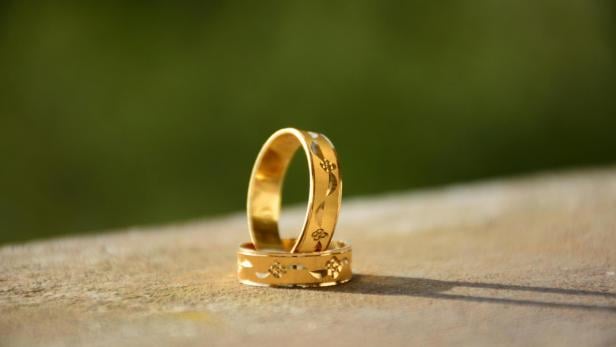 Zwei goldene Ringe mit eingravierten Blumenmustern stehen auf einer Oberfläche vor unscharfem grünem Hintergrund.