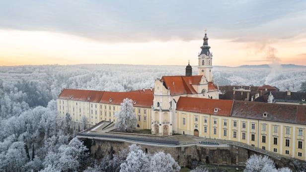Das Stift Altenburg mit rotem Dach und Kirchturm liegt inmitten einer winterlichen, schneebedeckten Landschaft.