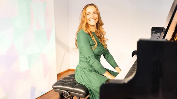 Frau in grünem Kleid sitzt lächelnd an einem schwarzen Flügel in hellem Raum.
