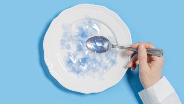 Ein Teller mit kleinen Mikroplastikteilchen und eine Hand, die einen Löffel hineinhält.