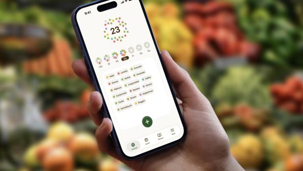 Hand hält Smartphone mit geöffneter Ernährungs-App vor unscharfem Gemüse-Hintergrund.