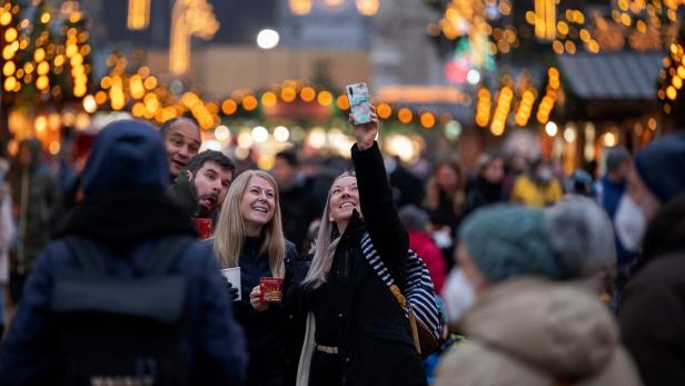 Auf einem Weihnachtsmarkt macht eine Frau ein Foto mit ihrem Handy.