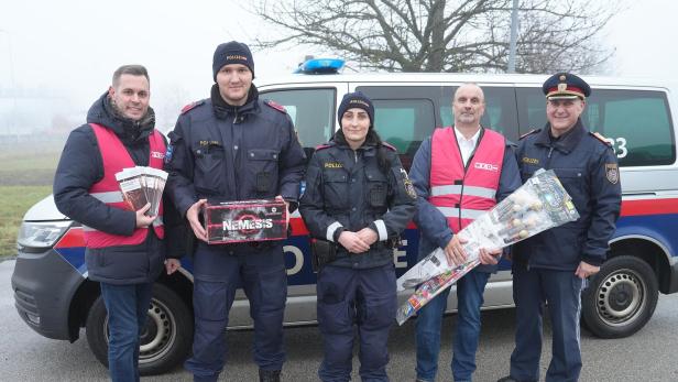 Fünf Personen, darunter Polizisten und zwei Männer mit pinken Westen, stehen vor einem Polizeiauto und halten Feuerwerkskörper und Flyer.