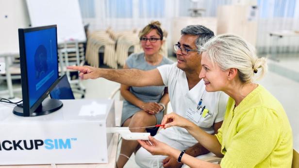 Drei Personen bedienen gemeinsam einen medizinischen Simulator und betrachten konzentriert den Monitor.