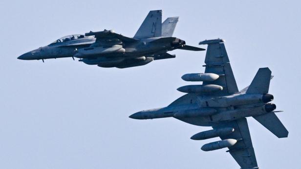 Zwei Militärjets fliegen dicht nebeneinander am Himmel, beide mit sichtbarer Bewaffnung und Zusatztanks.