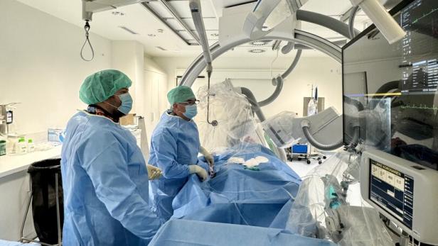 Zwei Personen in OP-Kleidung führen einen medizinischen Eingriff an einer liegenden Person mit moderner Technik durch.