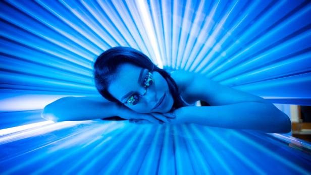 Eine Frau mit Schutzbrille liegt in einem Solarium unter blauem Licht.