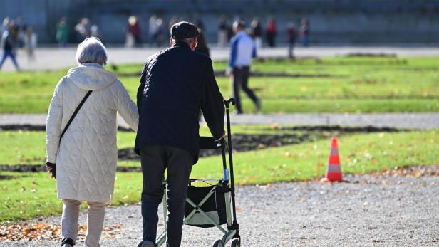 Ein älteres Paar geht im Park spazieren, der Mann mit einem Rollator.