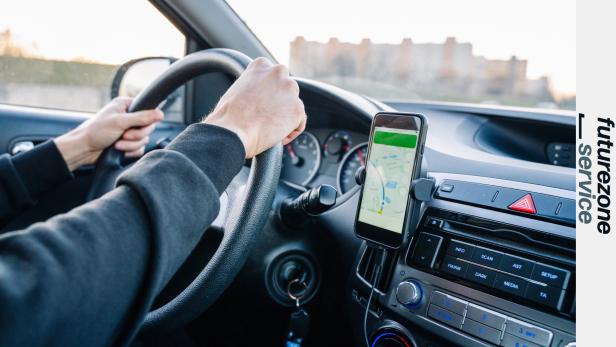 Eine Person steuert ein Auto, während Google Maps auf einem Smartphone zur Navigation genutzt wird.