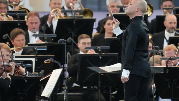 Dirigent mit erhobenem Taktstock leitet ein Orchester.  