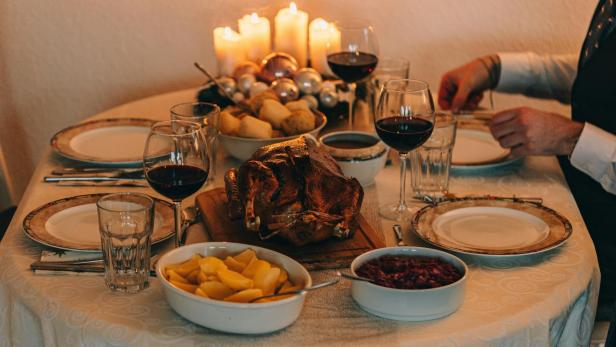 Festlich gedeckter Tisch mit Gänsebraten, Rotwein, Kartoffeln, Rotkohl, Kerzen und zwei Personen beim Abendessen.