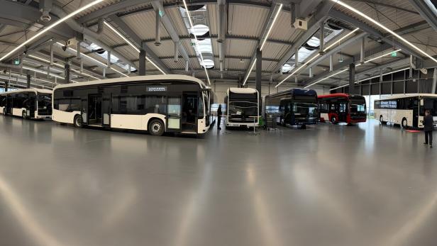 Mehrere moderne Linienbusse stehen in einer großen, hellen Halle mit hohen Decken und viel Tageslicht.