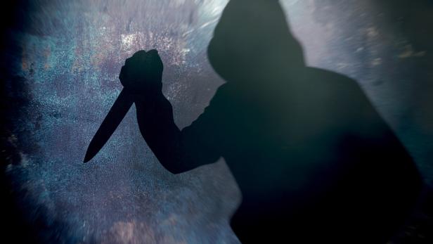 Eine dunkle Silhouette hält ein Messer vor einem gesprenkelten Hintergrund.