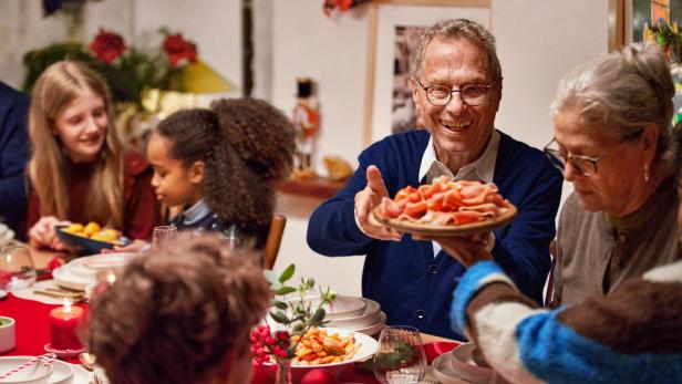 Mehrere Generationen sitzen an einem festlich gedeckten Tisch und teilen gemeinsam Essen in fröhlicher Stimmung.