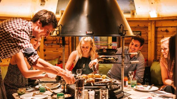 Menschen grillen gemeinsam an einem Tisch in eine Holzhütte.